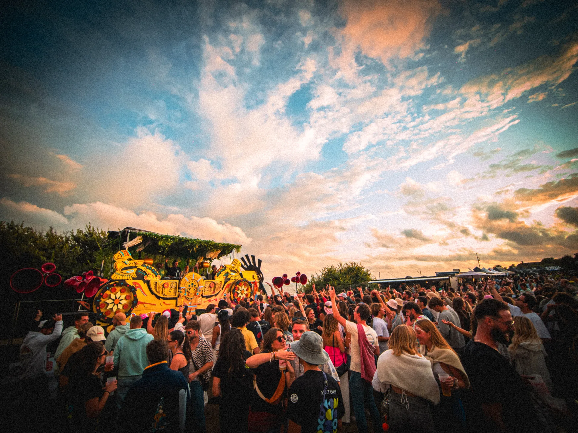 Ambiance dorée et foule animée au coucher du soleil sur le site du Flyin'Festival